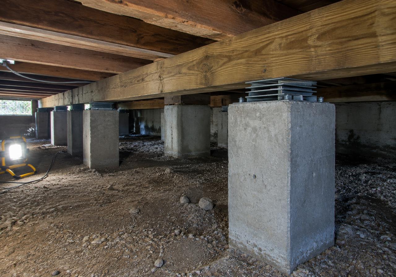 Illustrative crawlspace with concrete piers and shimmed support beams under a home